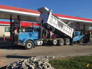 dump truck and paver install asphalt at convenience store
